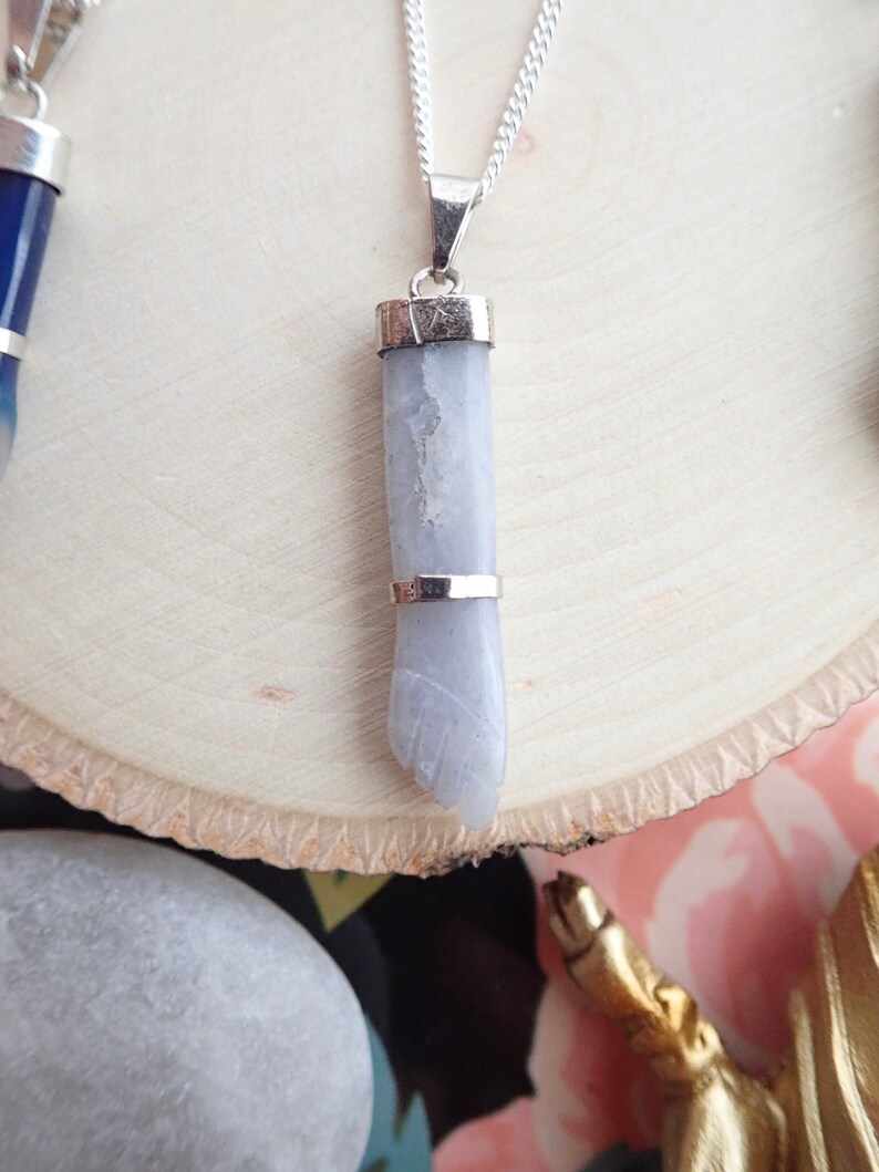May include: A silver chain necklace with a light gray stone pendant. The pendant is shaped like a hand and has a silver band around the top.
