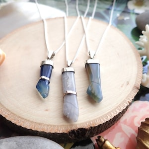 May include: Three silver necklaces with blue and white agate pendants shaped like hands. The pendants are on a wooden surface.