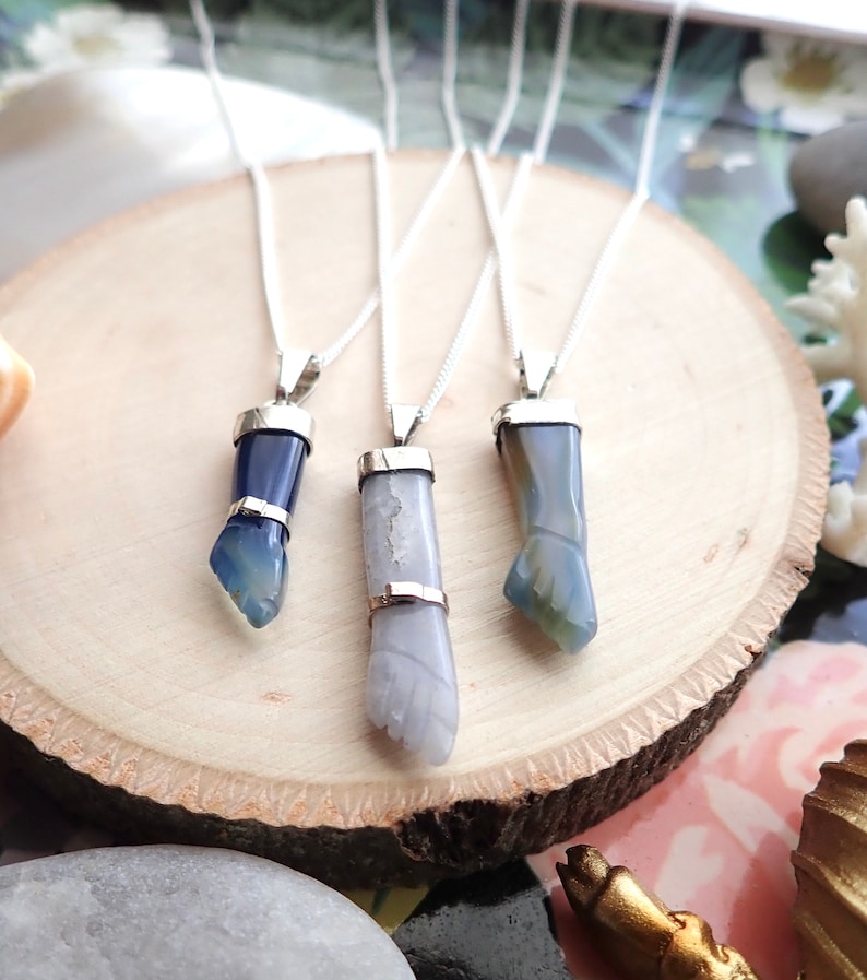 May include: Three silver necklaces with blue and white agate pendants shaped like hands. The pendants are on a wooden surface.