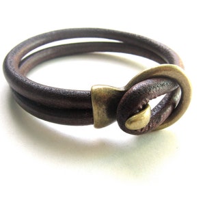 May include: A brown leather bracelet with a brass clasp. The bracelet is double-layered and has a simple design.