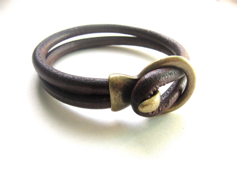 May include: A brown leather bracelet with a brass clasp. The bracelet is double-layered and has a simple design.
