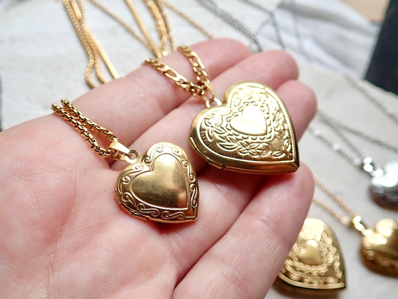 Pode incluir: Dois colares de ouro com pingentes em forma de cora&ccedil;&atilde;o com designs intrincados. Os pingentes est&atilde;o abertos e mostram um interior dourado liso.