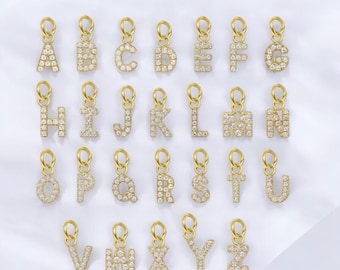 May include: A set of 26 gold-toned initial charms, each letter is encrusted with clear crystals. The charms are arranged in alphabetical order on a white surface.  Waterproof Crystal Initial Charms.