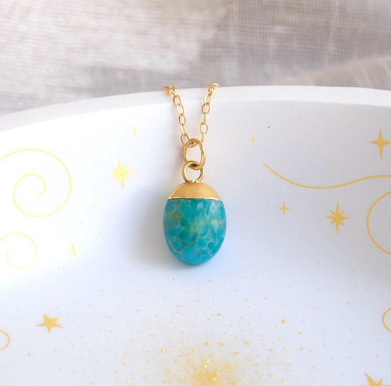 Peut inclure: Un collier &agrave; cha&icirc;ne dor&eacute;e avec un pendentif turquoise. Le pendentif est de forme ovale avec un capuchon dor&eacute;. La pierre turquoise pr&eacute;sente un motif mouchet&eacute; et est d'un bleu-vert vif. Le collier est pr&eacute;sent&eacute; sur une surface blanche.
