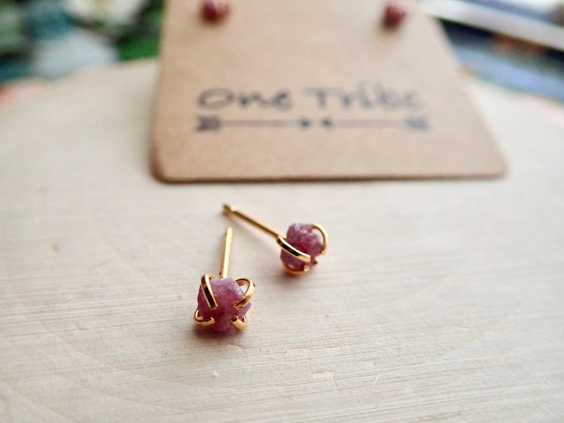 Puede incluir: Un par de pendientes de bot&oacute;n de oro con piedras rosadas crudas, parecidas a cristales, engastadas en una jaula de alambre de oro.