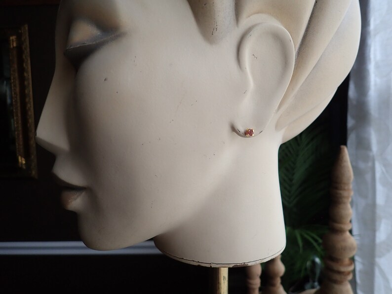 Puede incluir: Primer plano de la oreja de un maniqu&iacute; con un peque&ntilde;o pendiente redondo de piedra roja.