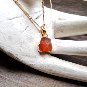 May include: A gold chain necklace with a pendant made of a raw, orange carnelian stone.