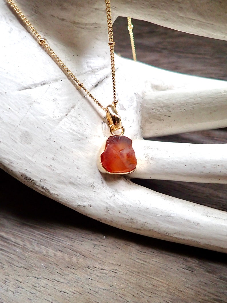 May include: A gold chain necklace with a pendant made of a raw, orange carnelian stone.