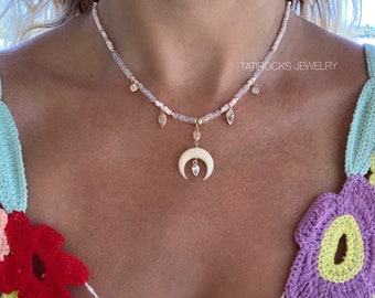 May include: A delicate white beaded necklace with a crescent moon pendant and small crystal accents. The necklace is worn by a person with a colorful crocheted top. The text "TATIROCKS JEWELRY" is visible in the image.