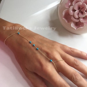 May include: A gold chain bracelet with turquoise beads, designed to be worn as a hand chain with a ring that fits on the finger.