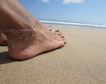 May include: A woman's foot with a turquoise and silver ankle bracelet on a sandy beach.