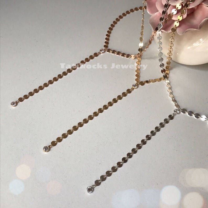 May include: Three gold, silver, and rose gold necklaces with small round discs and a single clear rhinestone at the end of each chain.