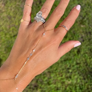 May include: A gold chain bracelet with small diamonds, worn on a hand with a large diamond ring and several other rings.