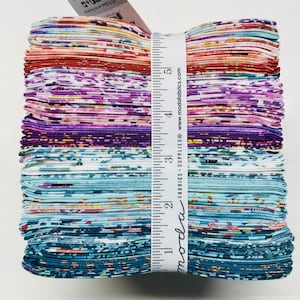 Könnte beinhalten: Ein Stapel bunter Stoffquadrate mit einem Blumenmuster. Der Stoff wird mit einem Lineal gemessen, auf dem "moda fabrics + supplies" und "www.modafabrics.com" steht.