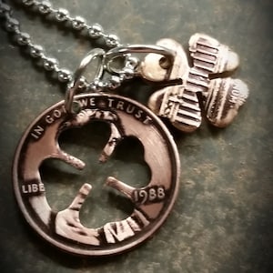 May include: A silver chain necklace with a copper-colored pendant featuring a four-leaf clover design. The pendant is a 1988 US penny with the center cut out to create the clover shape. The necklace also has a smaller copper-colored four-leaf clover charm.