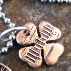 May include: A copper four-leaf clover charm necklace with a silver ball chain. The clover charm has a detailed design and is attached to the chain with a silver ring.