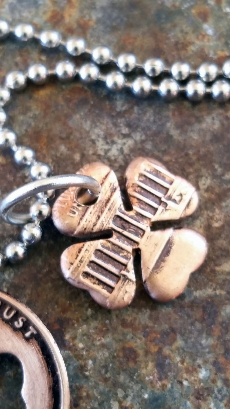 May include: A copper four-leaf clover charm necklace with a silver ball chain. The clover charm has a detailed design and is attached to the chain with a silver ring.