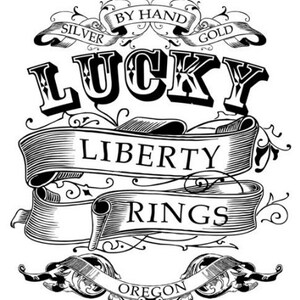 May include: Black and white illustration of a logo for Lucky Liberty Rings. The logo features a stylized banner with the words "Lucky Liberty Rings" and the text "By Hand Silver Gold" and "Oregon" in a decorative font.