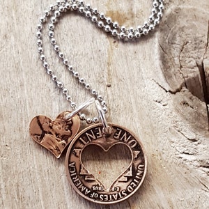 Op de afbeelding: Een zilveren ketting met een koperen hanger met een hart dat uit een cent-munt is geknipt. De munt heeft de tekst "ONE CENT" en "UNITED STATES OF AMERICA" met het jaar "1985" en "E PLURIBUS UNUM". Een kleinere koperen hartbedel is aan de munt bevestigd.