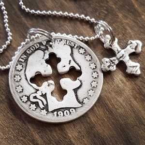 May include: A silver necklace with a pendant featuring a cross cut out of a 1909 US coin with the inscription "In God We Trust". A smaller silver cross pendant hangs from the chain.