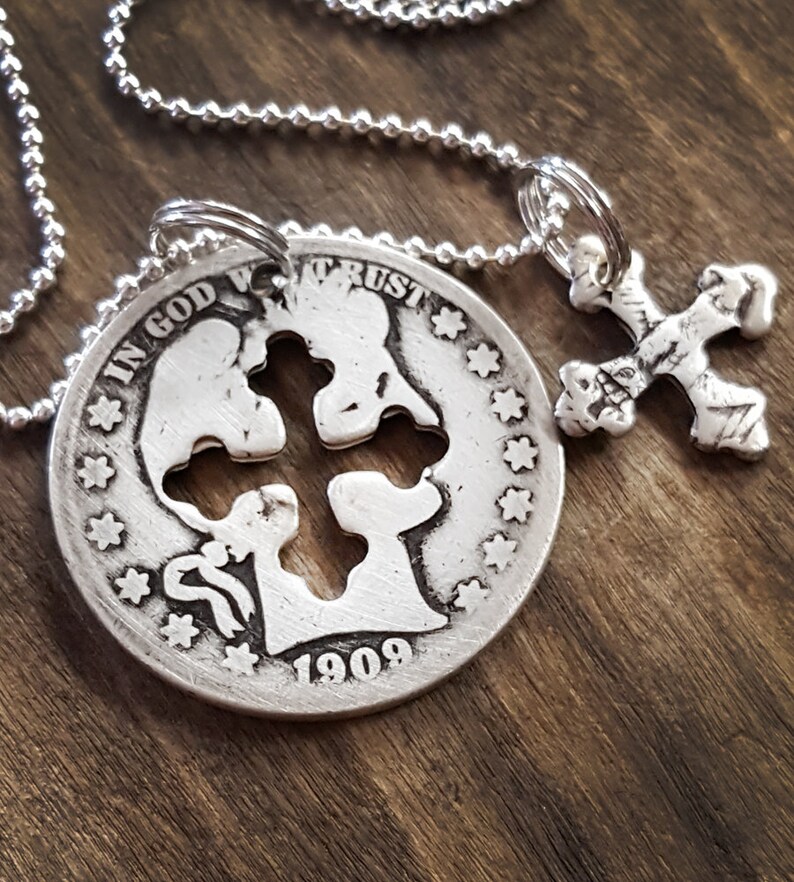 May include: A silver necklace with a pendant featuring a cross cut out of a 1909 US coin with the inscription "In God We Trust". A smaller silver cross pendant hangs from the chain.