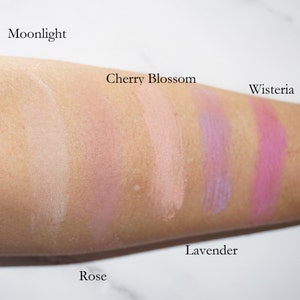 May include: Swatches of six different shades of blush on a person's arm. The shades are labeled "Moonlight", "Cherry Blossom", "Rose", "Lavender", "Wisteria", and "Rose".