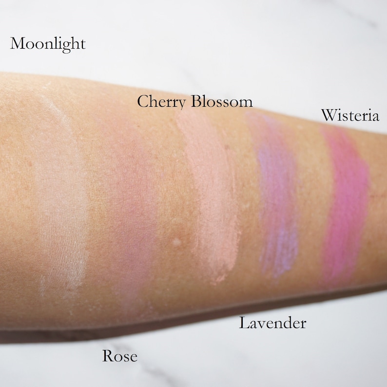 May include: Swatches of six different shades of blush on a person's arm. The shades are labeled "Moonlight", "Cherry Blossom", "Rose", "Lavender", "Wisteria", and "Rose".