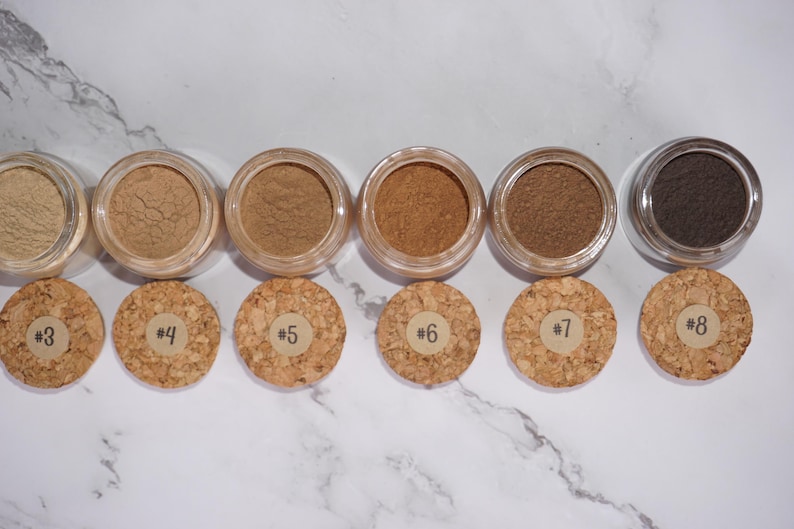 May include: A collection of six small, clear jars filled with various shades of brown powder, each with a cork lid. The lids are numbered from #3 to #8. The powders range in color from light beige to dark brown.