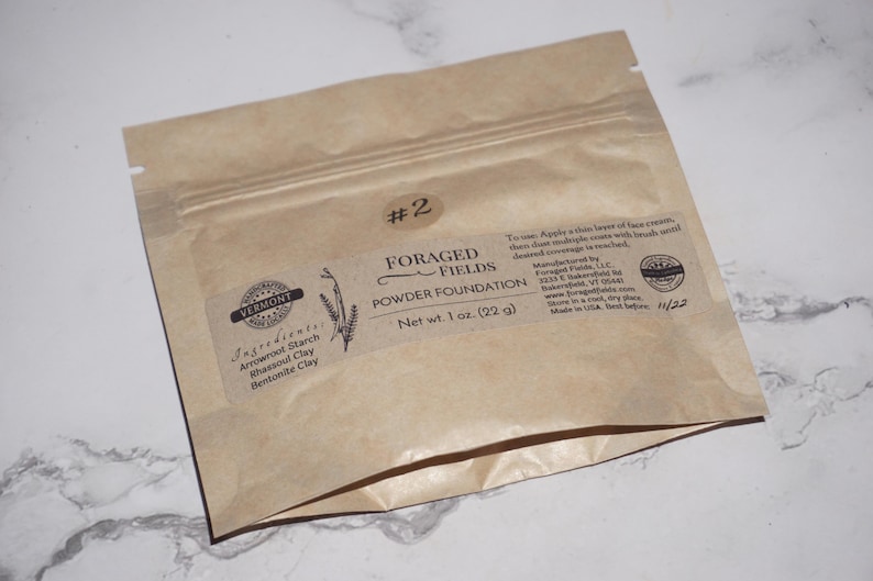 May include: A brown paper packet of Foraged Fields Powder Foundation, net weight 1 oz (22 g). The label includes the ingredients: arrowroot starch, rhassoul clay, and bentonite clay. The packet has a zip closure and the text "#2".