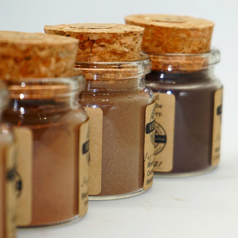 May include: Close-up of several small glass jars filled with brown powders, each sealed with a cork stopper. The jars have small, rectangular labels. The powders vary in shade from light brown to dark brown.