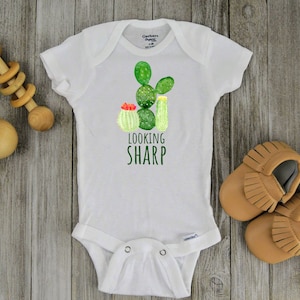 May include: White baby onesie with a green cactus graphic and the text "Looking Sharp".