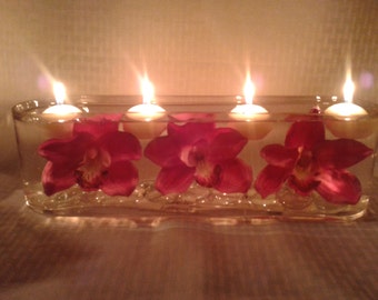 Long glass vase with large purple flowers, crystals, and floating candles