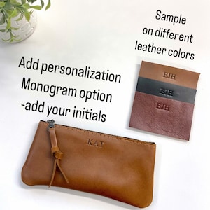 May include: A brown leather pencil case with a zipper closure and a monogrammed "KAT" on the front. The image shows a sample of the case in different leather colors with the initials "EJH" embossed on each.