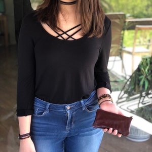 May include: A woman wearing a black long-sleeved shirt with a criss-cross neckline, blue jeans, and a brown leather wallet.