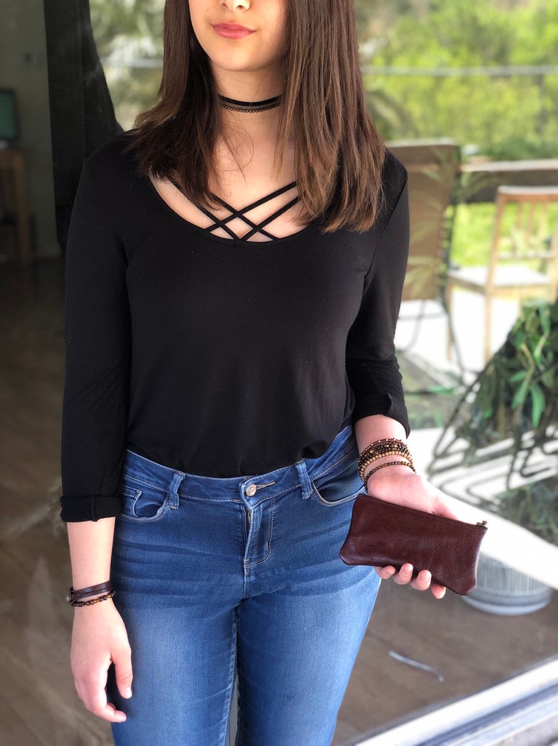 May include: A woman wearing a black long-sleeved shirt with a criss-cross neckline, blue jeans, and a brown leather wallet.