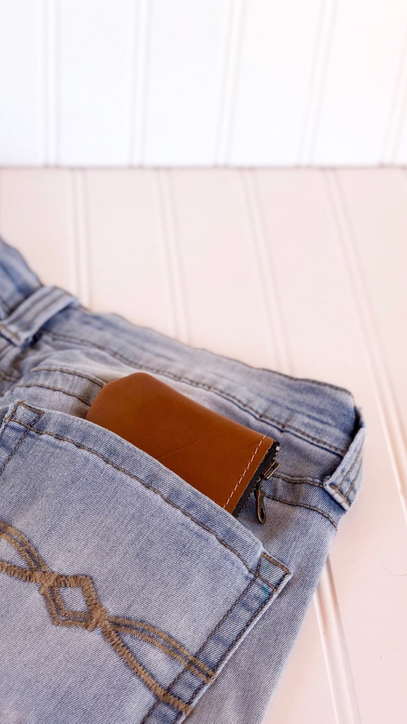 May include: A brown leather wallet with a zipper is tucked into the back pocket of a pair of light blue jeans.