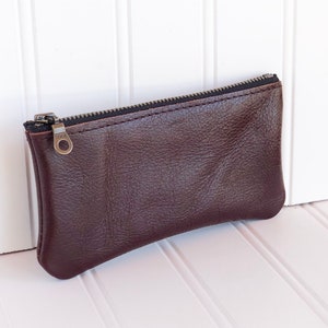 May include: A brown leather zippered pouch with a silver zipper pull.