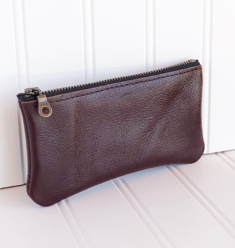 May include: A brown leather zippered pouch with a silver zipper pull.