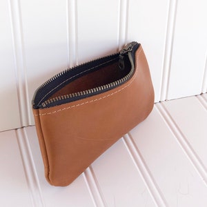 May include: A brown leather zippered pouch with a black zipper. The pouch is open and the inside is visible.