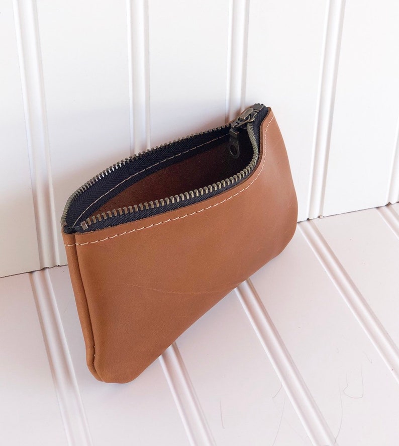 May include: A brown leather zippered pouch with a black zipper. The pouch is open and the inside is visible.
