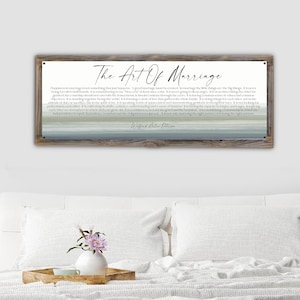 May include: A framed wall art piece with the text "The Art Of Marriage" in elegant script. The artwork features a quote by Wilfred Arlan Peterson, set against a serene, watercolor-style background of muted blues and greens.