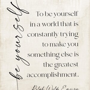 May include: A rectangular print with a beige background and black text. The text reads "To be yourself in a world that is constantly trying to make you something else is the greatest accomplishment." The author is Ralph Waldo Emerson.