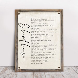 May include: A vintage-style print with lyrics from the song "Shallow" by Lady Gaga and Bradley Cooper. The lyrics are printed in black ink on a white background with a distressed wood frame.