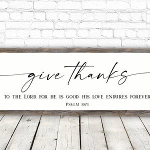 May include: A white wooden sign with black text that reads "give thanks to the Lord for he is good. His love endures forever. Psalm 107:1".