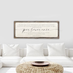 May include: A wooden sign with a white background and black text. The sign reads "Therefore, since we are surrounded by such a great cloud of witnesses, let us throw off everything that hinders and the sin that so easily entangles. And let us run with perseverance the race marked out for us, fixing our eyes on Jesus, the pioneer and perfecter of faith. Hebrews 12:1-2 Something Promised".