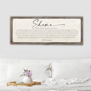 May include: A rustic wooden sign with a white background and black text. The sign features the word "Shema" in a decorative script font. The text includes a passage from Deuteronomy 6, which reads: "Hear, O Israel: The Lord our God, the Lord is one. You shall love the Lord your God with all your heart, and with all your soul, and with all your might. The words which I command you this day shall be in your heart. You shall teach them diligently unto your children, and shall talk of them when you sit in your house, and when you walk by the way, and when you lie down, and when you rise up. You shall fear the Lord your God, and serve him, and shall swear by his name. You shall not go after other gods, the gods of the people which are round about you. For the Lord is our God, and the Lord is one."