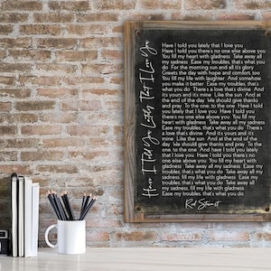 May include: A black framed sign with a white background and a handwritten song lyric by Rod Stewart. The lyrics are "Have I told you lately that I love you. You fill my heart with gladness. Take away all my sadness. Ease my troubles. That's what you do."