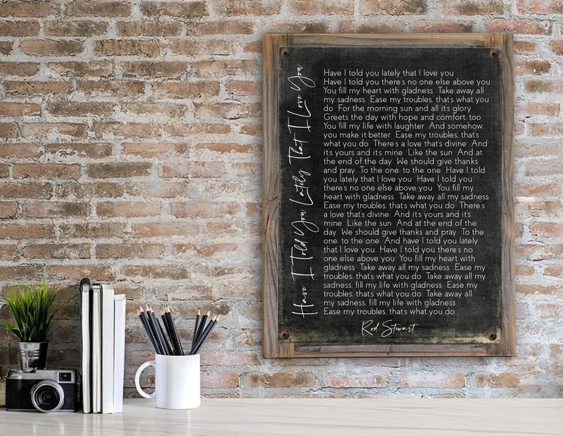 May include: A black framed sign with a white background and a handwritten song lyric by Rod Stewart. The lyrics are "Have I told you lately that I love you. You fill my heart with gladness. Take away all my sadness. Ease my troubles. That's what you do."