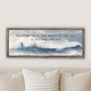May include: A rectangular wall art piece with a wooden frame. The artwork features a dramatic image of ocean waves and the text "Mightier than the waves of the sea is His love for you" from Psalm 93:4.