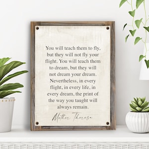 May include: A rustic wooden sign with a white background and a quote by Mother Theresa: "You will teach them to fly, but they will not fly your flight. You will teach them to dream, but they will not dream your dream. Nevertheless, in every flight, in every life, in every dream, the print of the way you taught will always remain."